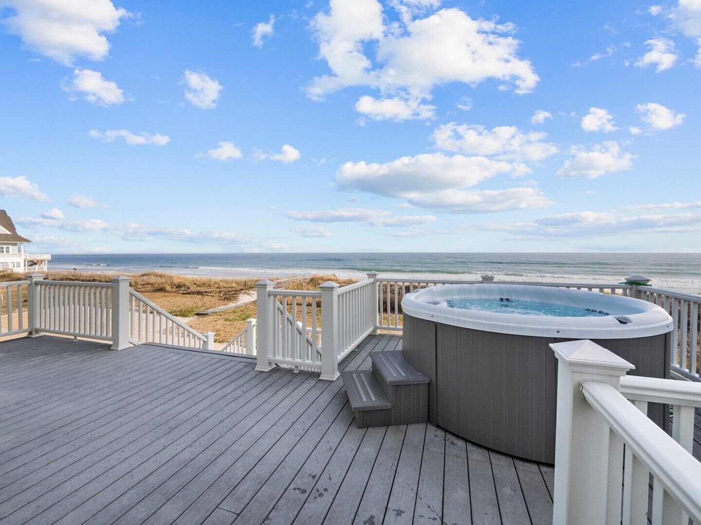 Eine Holzterrasse mit Whirlpool und Blick auf den Strand.