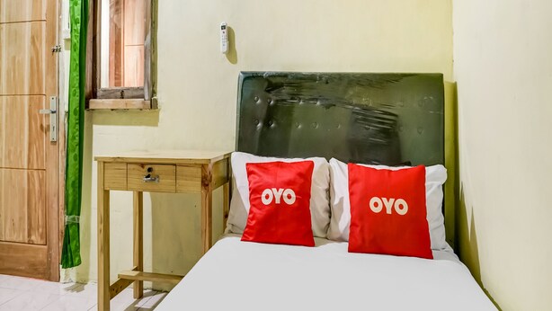 A room with a bed, a wooden wardrobe, a small table, and a green curtain. - OYO Life 91335 Micheline Family 2 Syariah (Karawang)