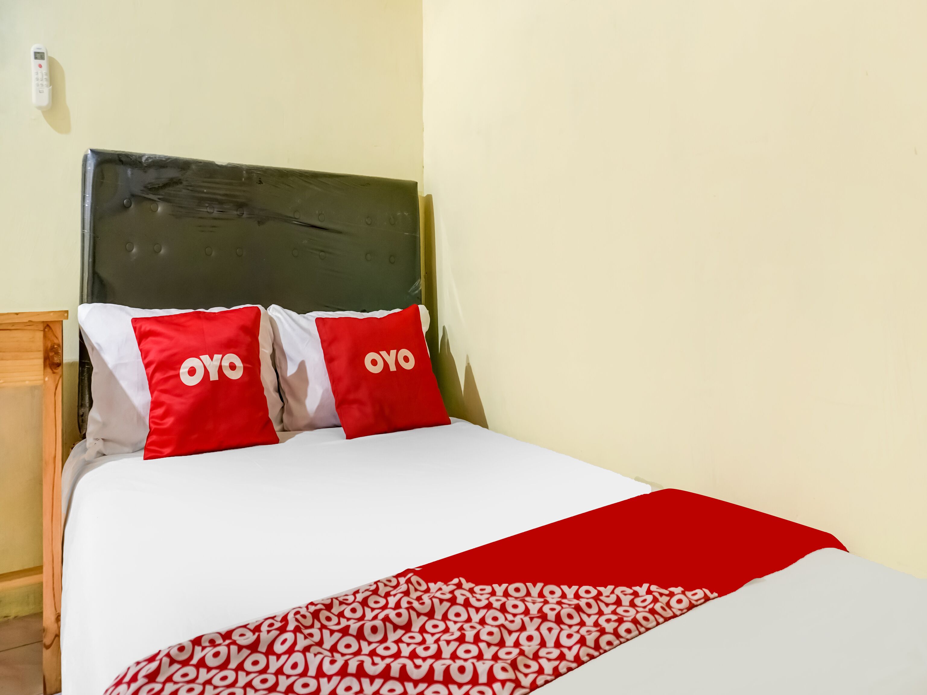 Un lit avec une couvre-lit blanche et rouge, deux oreillers rouges ornés du texte « OYO », et une tête de lit en bois.