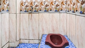 A bathroom with a blue patterned floor, a red toilet, and a wall decorated with fish and coral tiles. - OYO Life 91335 Micheline Family 2 Syariah (Karawang)