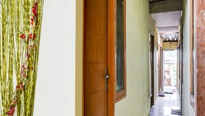 A hallway with a wooden door, a framed picture on the wall, and a view into an adjacent room. - OYO Life 91335 Micheline Family 2 Syariah (Karawang)
