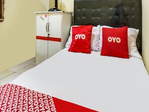 Hotellihuone, jossa on sänky, valkoiset vuodevaatteet sekä punavalkoiset kuviolliset tyynyt.