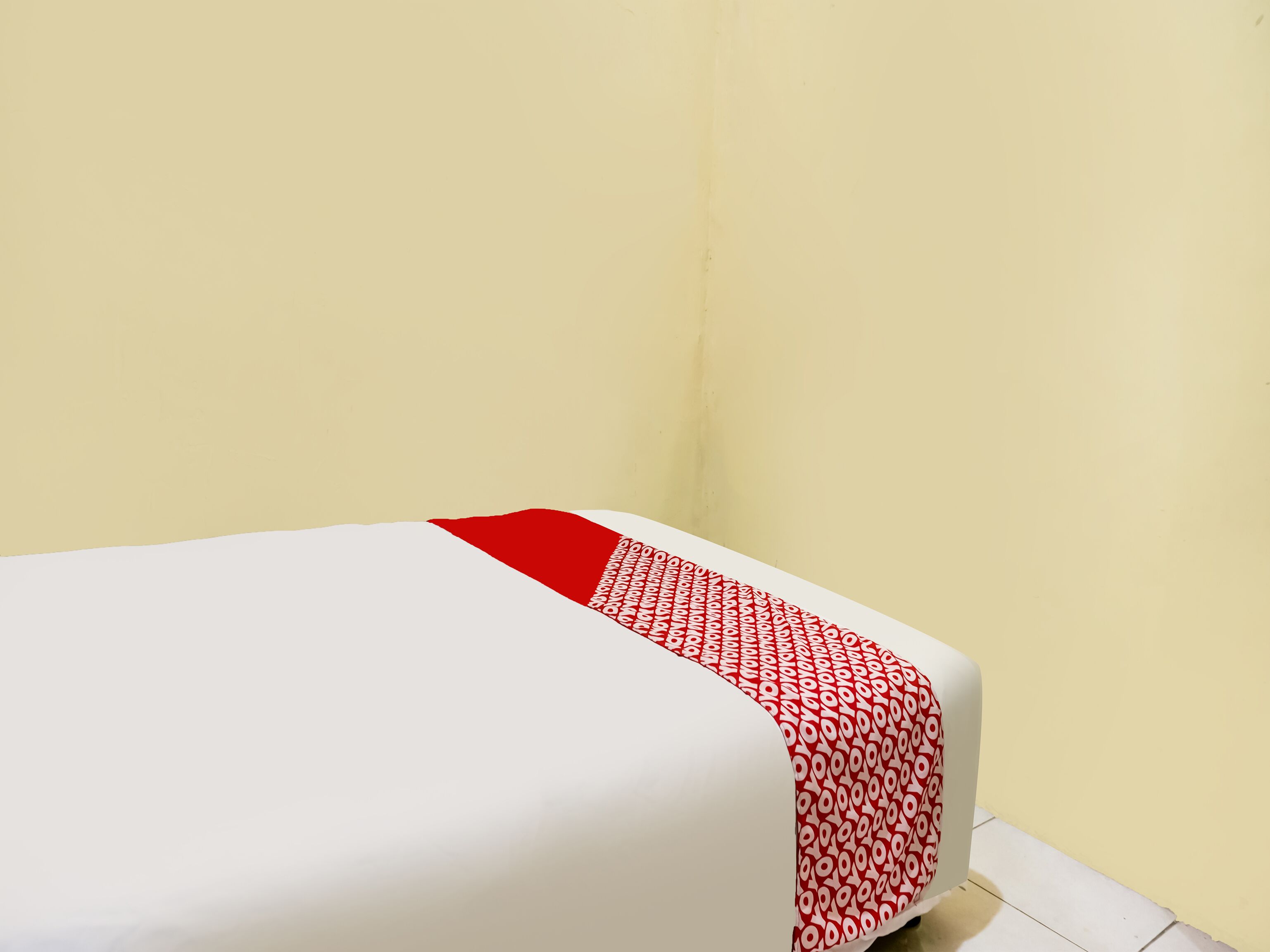 Un lit simple avec une couvre-lit à motifs rouges et blancs, dans une pièce aux murs de couleur jaune unie.