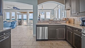 A spacious kitchen with dark cabinets, a dishwasher, and a coffee maker. There is a dining area with a view of the ocean. - Island Drive 4180 (North Topsail Beach)