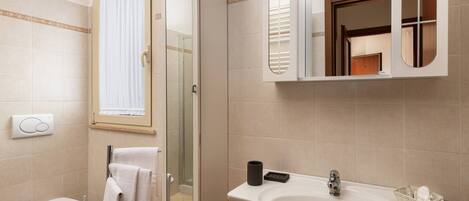 A bathroom with a toilet, a glass-enclosed shower, a sink with a mirror, and a window with curtains.