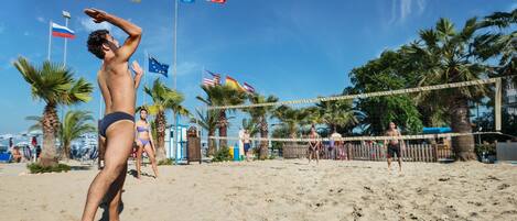 Un partido de voleibol de playa con jugadores y banderas al fondo.