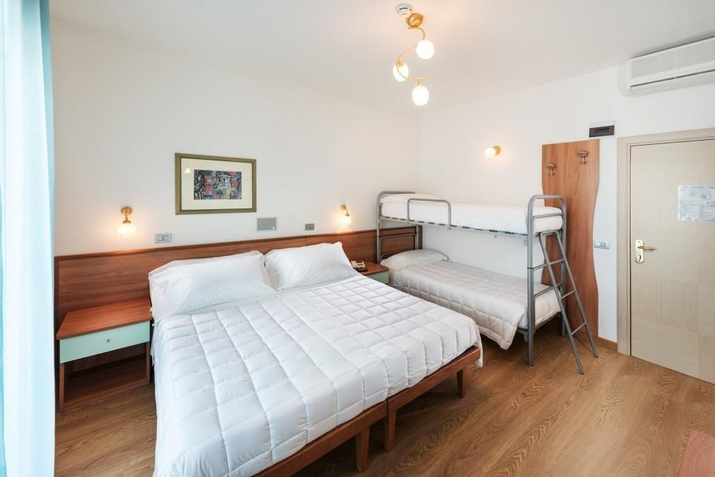 A room with a large bed, a smaller bed, a wooden bench, a ladder, and a door.