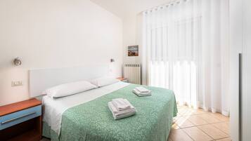 Habitación de hotel con cama, mesita de noche, cómoda, radiador y ventana con cortinas.