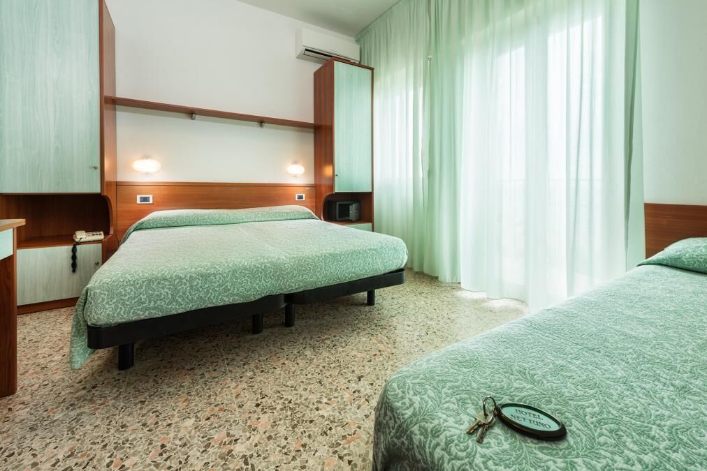A hotel room with two beds, a minibar, a desk, and a mirror.