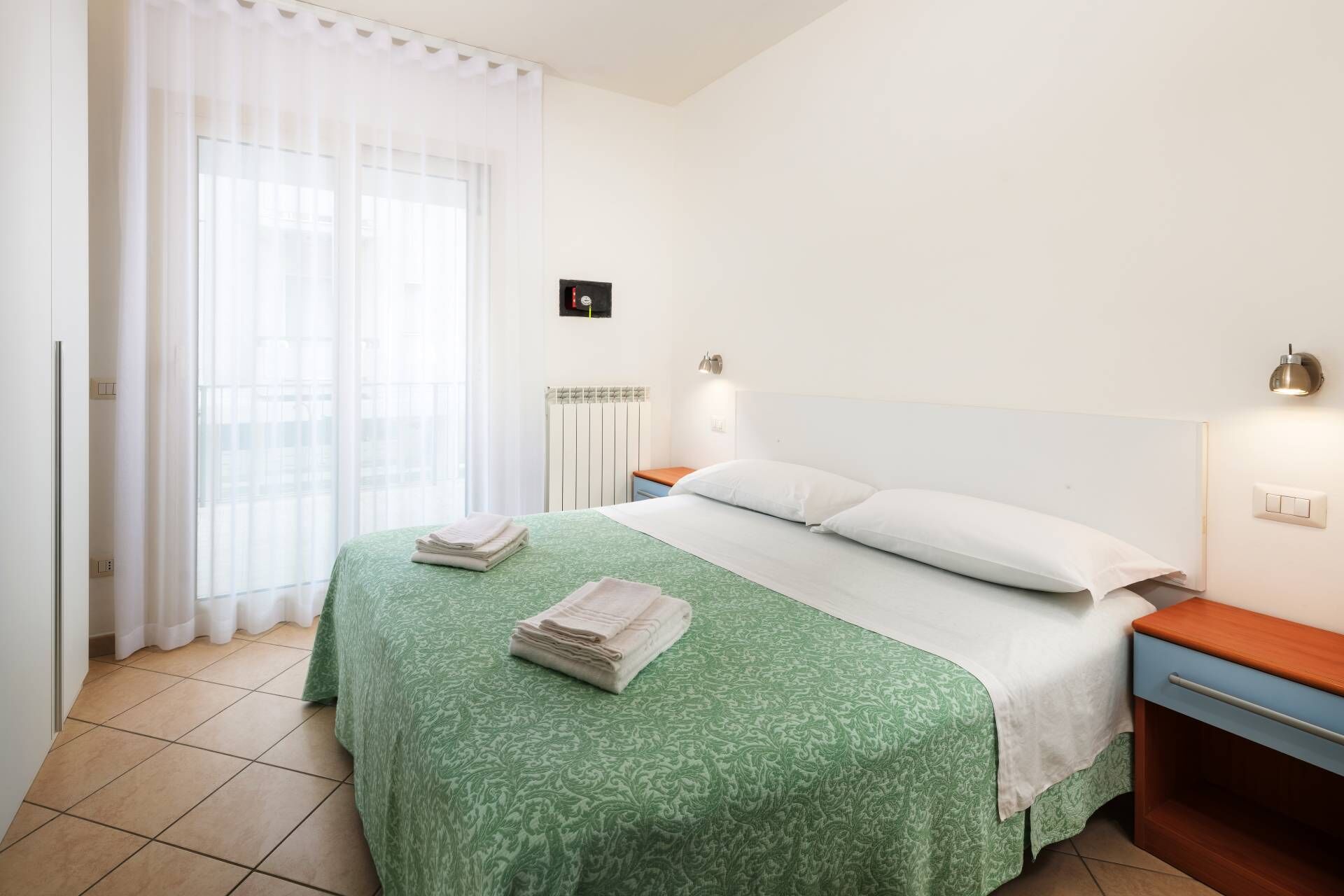 A hotel room with a bed, a nightstand, a lamp, and a window with curtains.