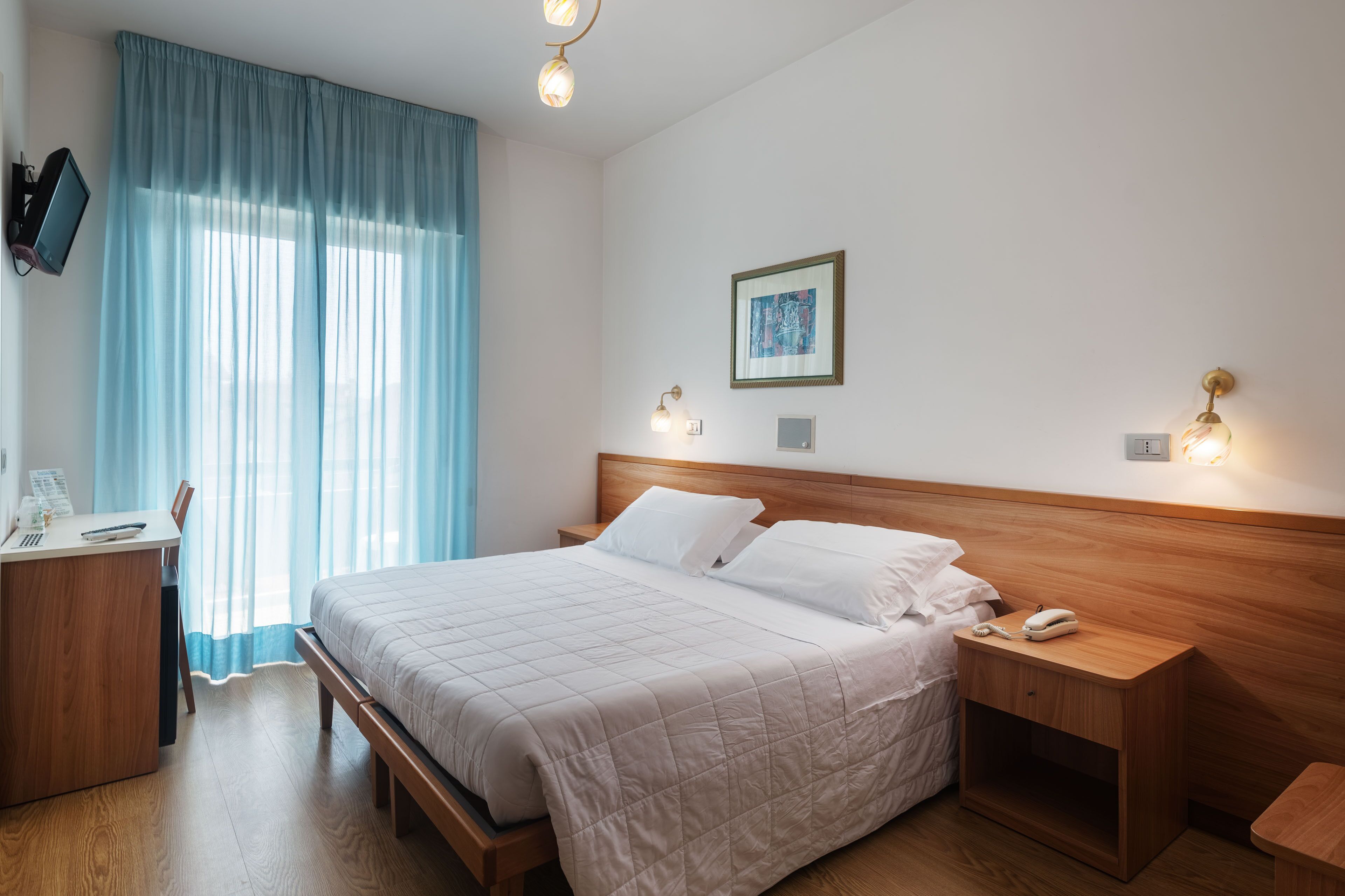 A neatly arranged hotel room with a bed, bedside table, and a desk with a chair.