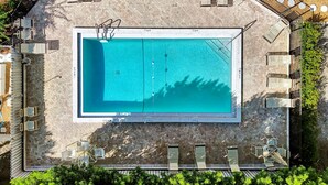 An aerial view of a rectangular swimming pool with a tiled deck surrounding it, equipped with lounge chairs and a sunshade structure. - Canal front Sanibel condo, short stroll to the Gulf of Mexico. (Sanibel)