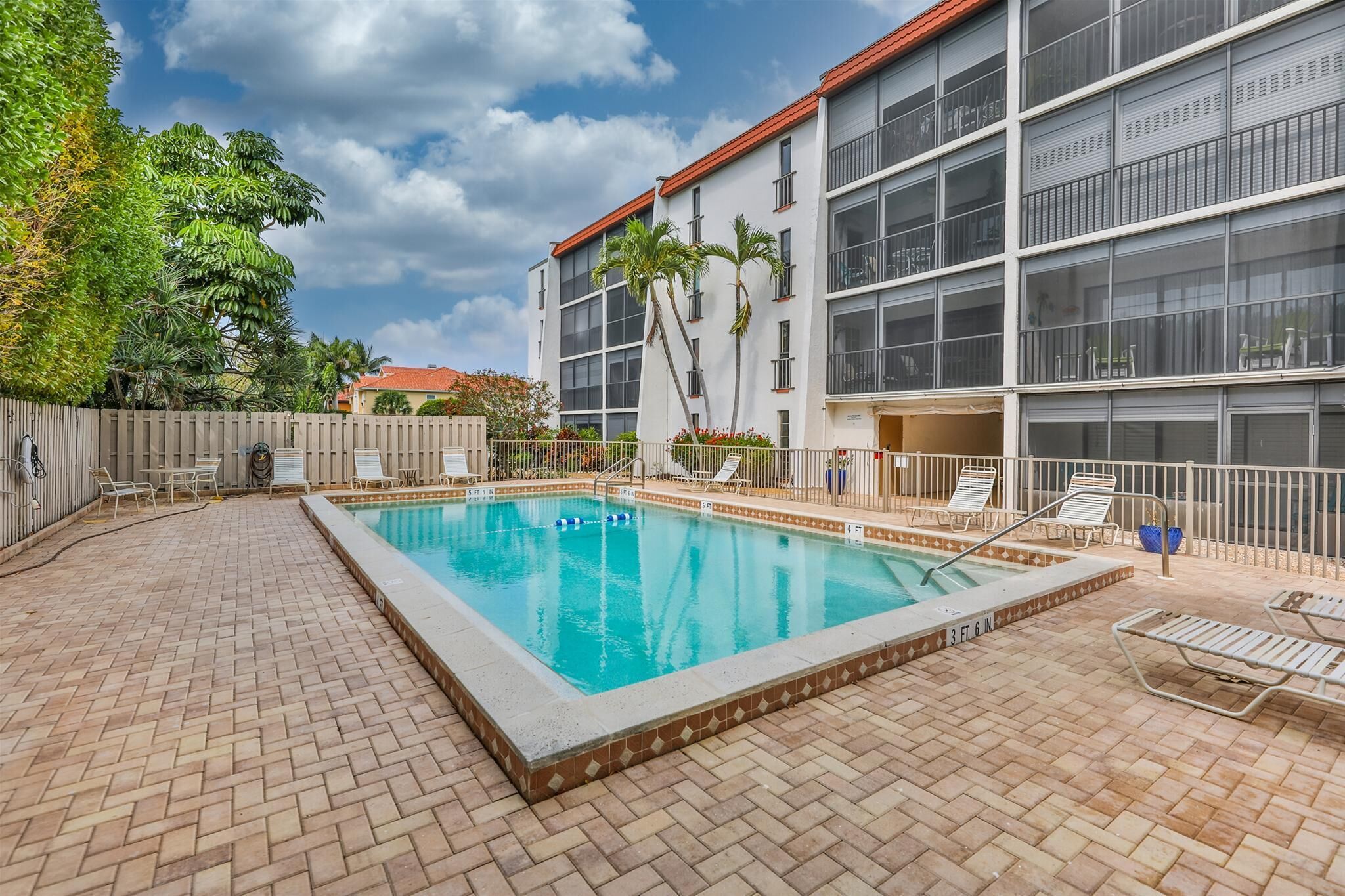Une piscine rectangulaire, bordée d’une terrasse carrelée, entourée de chaises longues et d’une clôture.