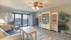 A living room with a ceiling fan, a sofa, a coffee table, a TV stand, and a large window with a view. - Canal front Sanibel condo, short stroll to the Gulf of Mexico. (Sanibel)