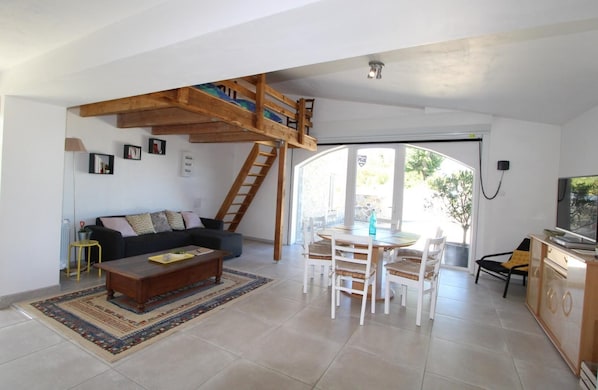 Un vaste espace de vie doté d’un haut plafond en bois, d’un canapé, d’une table basse, d’une table à manger avec des chaises et d’un téléviseur.