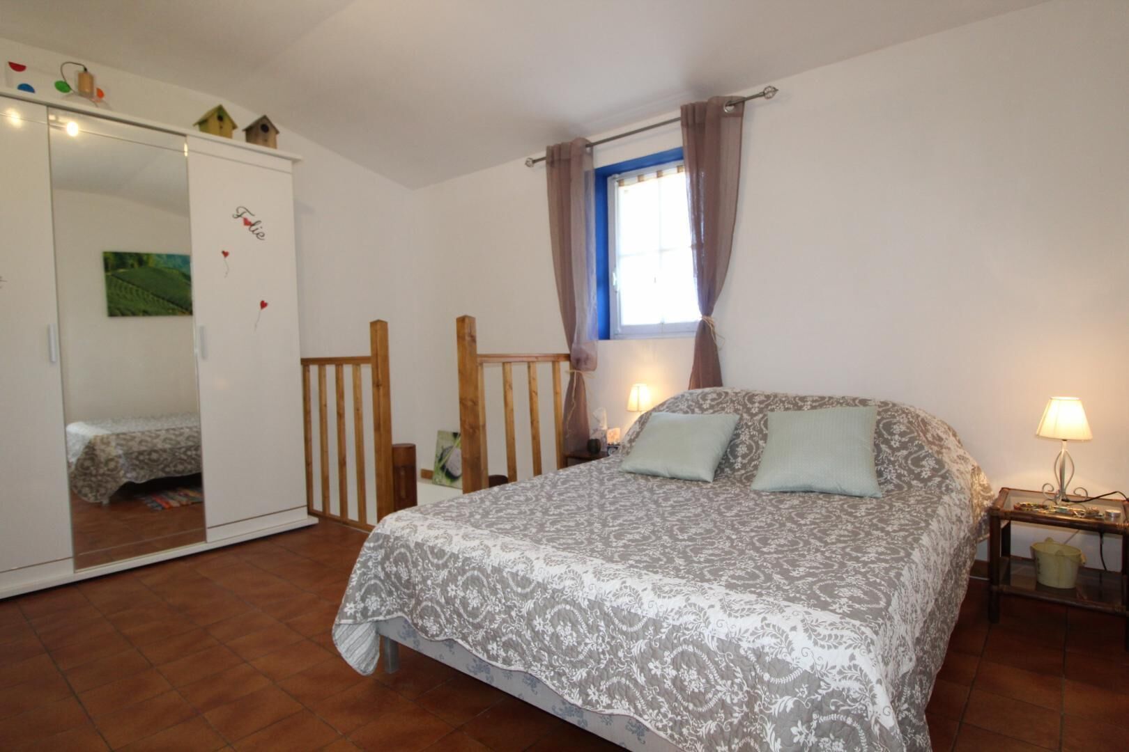 Une chambre à coucher comprenant un lit, une armoire, une fenêtre avec des rideaux et une table de chevet avec une lampe.