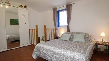 Une chambre à coucher comprenant un lit, une armoire, une fenêtre avec des rideaux et une table de chevet avec une lampe.