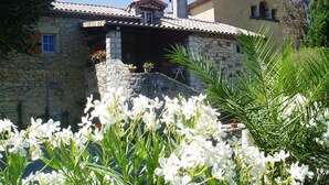 A stone building with a tiled roof, a chimney, and a small porch with potted plants. - MONLOUBIER (Villeneuve-de-Berg)