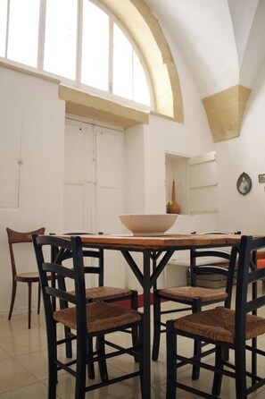 A dining area with a wooden table and chairs, a large window, and a white door. - Vacation home Caminanti - Historic center Lecce (Lecce)