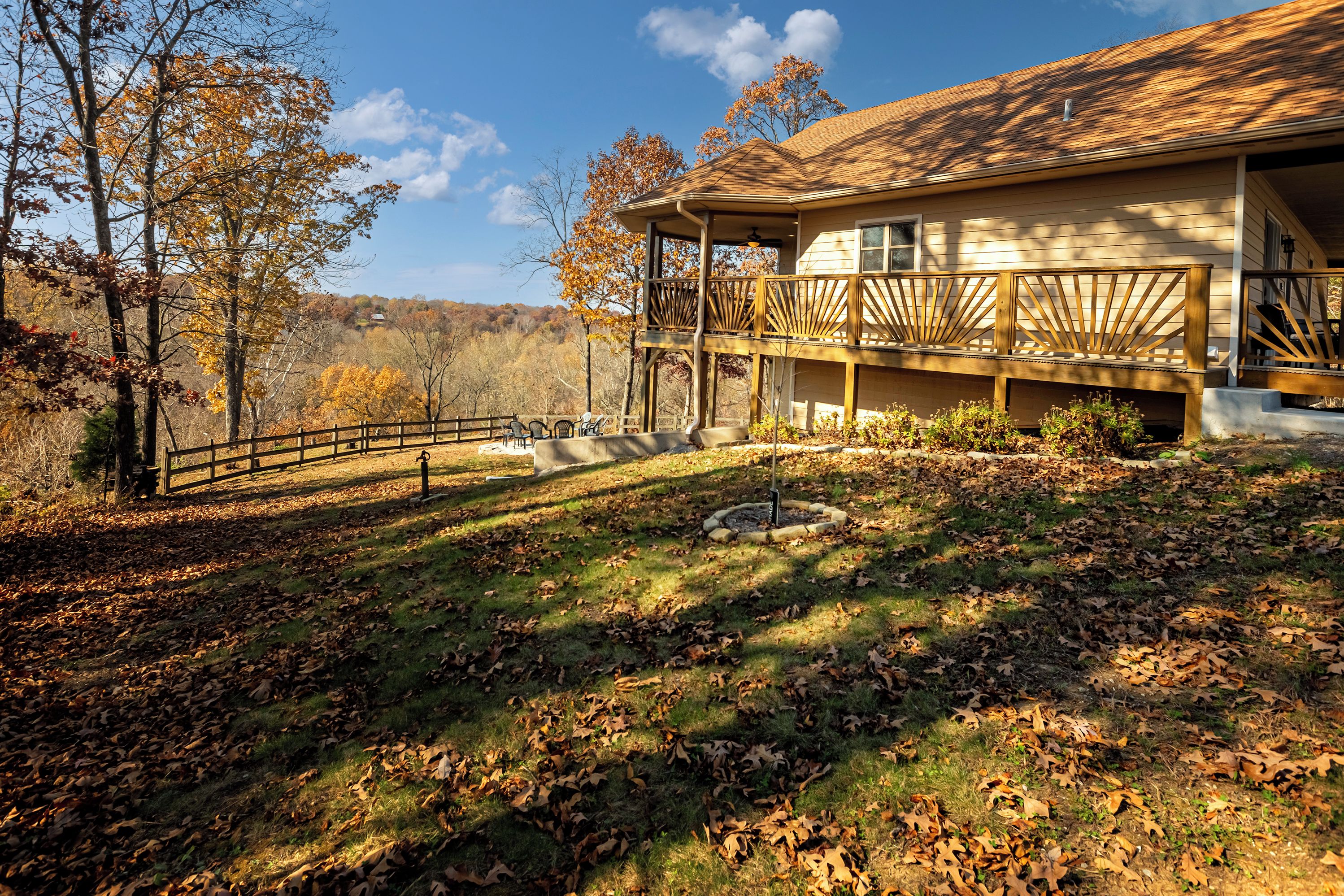 A two-story house with a balcony, surrounded by a wooden fence and a lawn with scattered leaves.