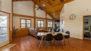 A spacious room with a wooden ceiling, a dining table with chairs, a sofa, and a fireplace.