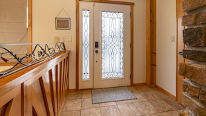 A wooden-finished hallway with a metal railing, a decorative door with a "HELLO" sign, and a stone wall.