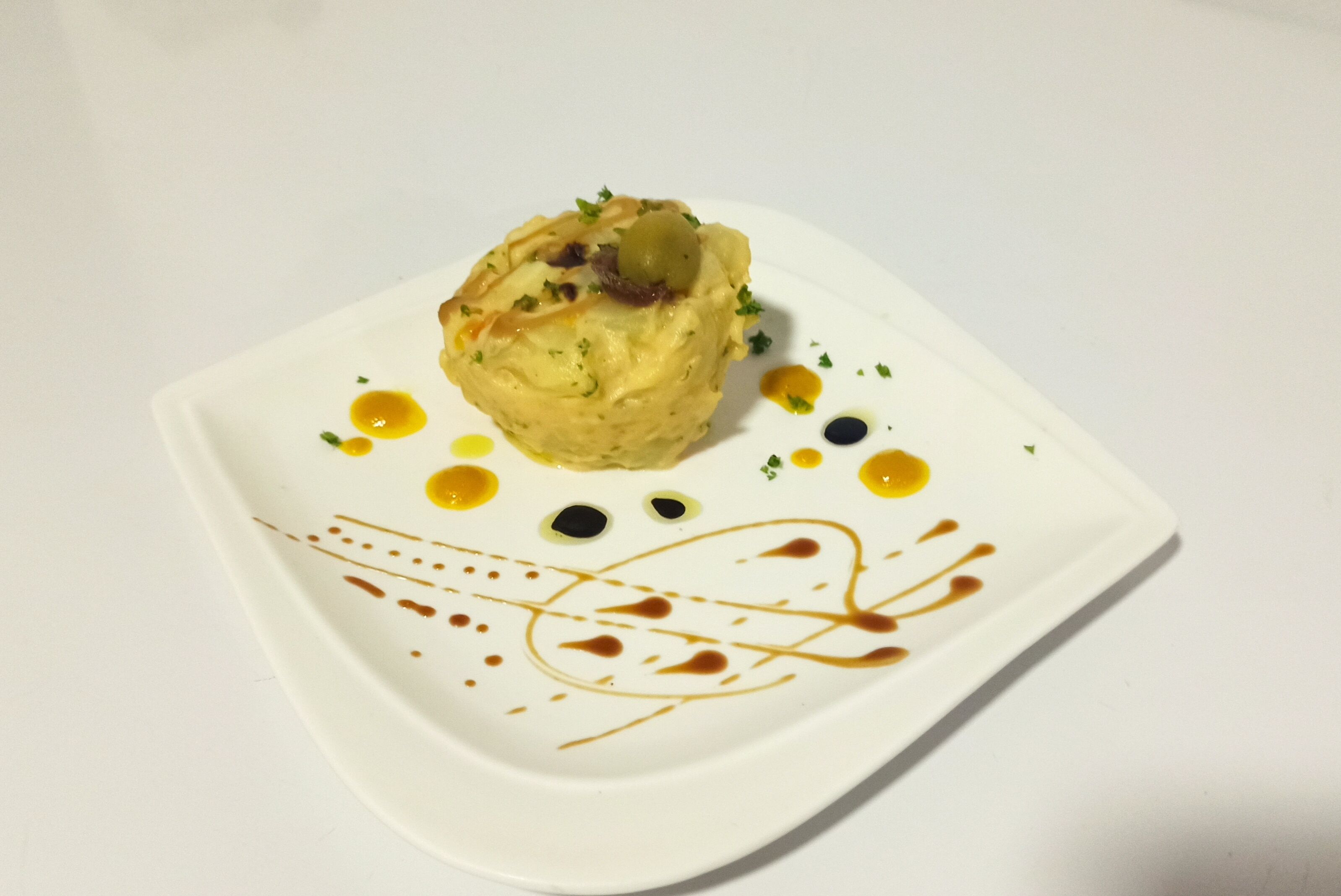 Plato blanco cuadrado con comida y delicados adornos de salsa.
