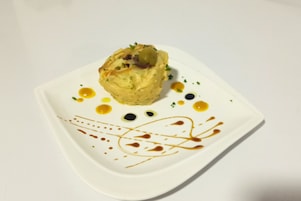 Plato blanco cuadrado con comida y delicados adornos de salsa.