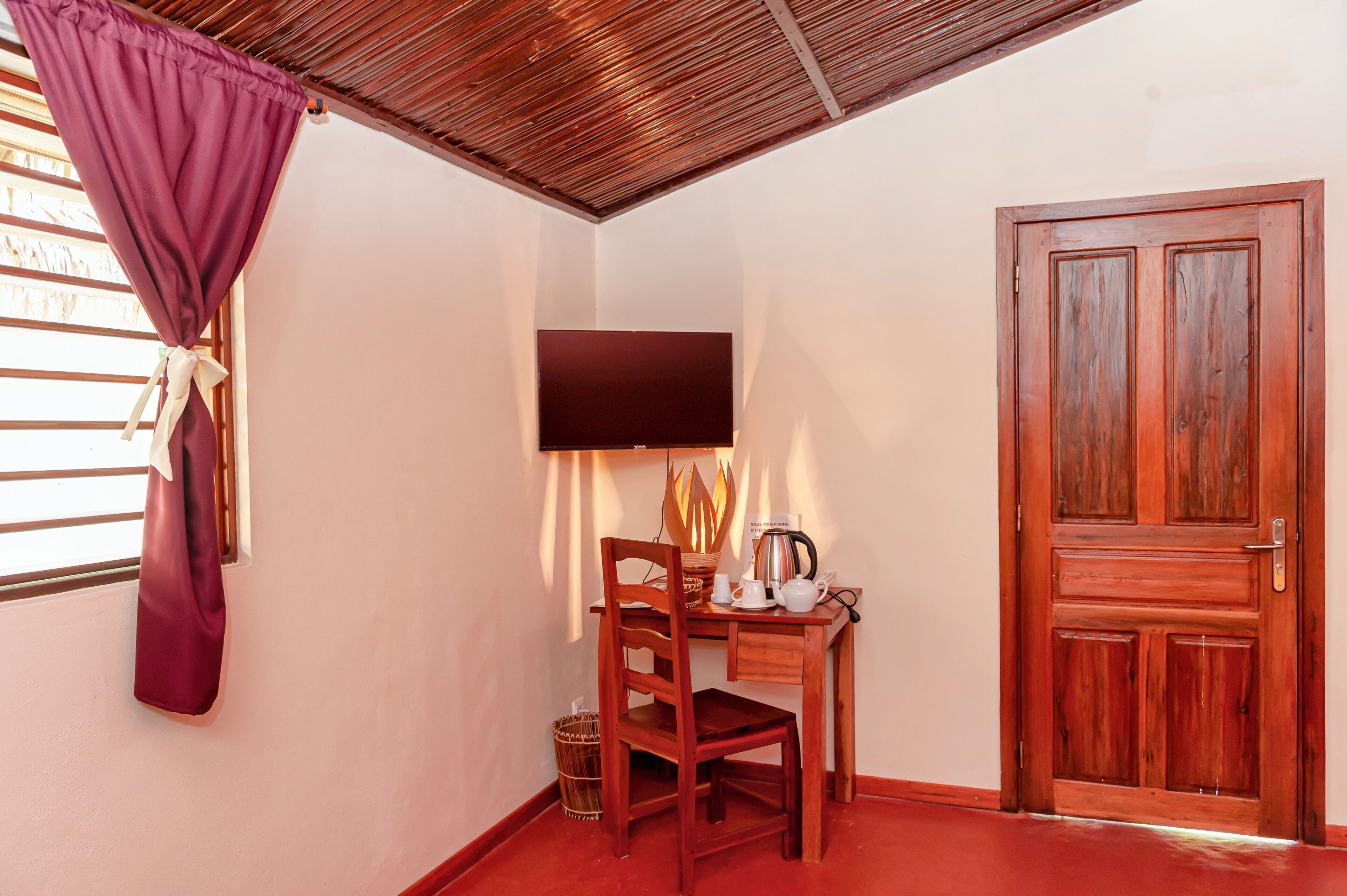 Una habitación con un escritorio de madera, una silla, un televisor montado en la pared y una puerta de madera.