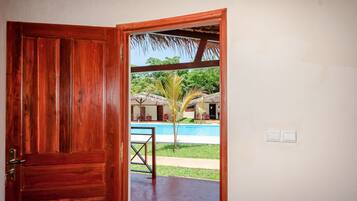 Una puerta de madera que da a una zona de piscina con una estructura de techo de paja y una pequeña palmera.