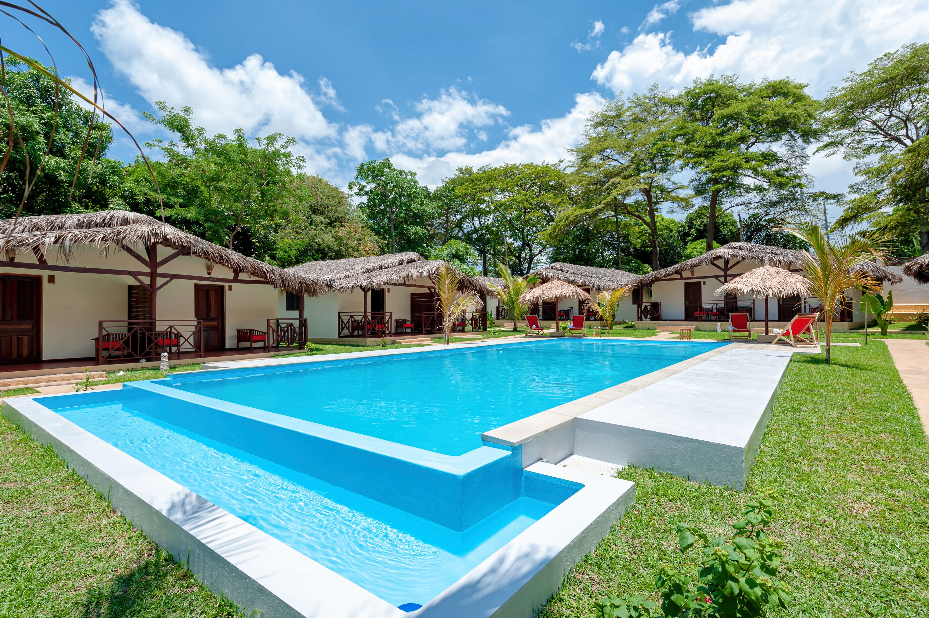 Una piscina rodeada de chozas con techo de paja, con mobiliario exterior y un exuberante paisaje verde.