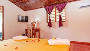 A hotel room with a bed, a TV, a wooden ceiling, and a window with curtains. - BLUE SKY RESORT (Nosy Be)
