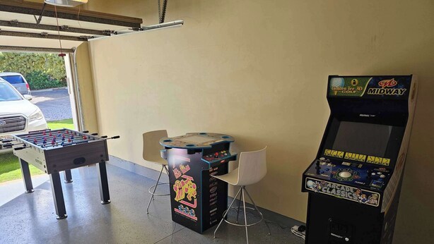 A garage with a foosball table, a 3D golf arcade machine, and a chair. - 4BR I Ground Floor Luxury Penthouse at The Villas | F100 (Koloa)