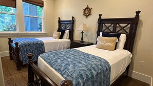 A bedroom with two beds, a ceiling fan, a ship's wheel decoration, and a window with a view of greenery. - 4BR I Ground Floor Luxury Penthouse at The Villas | F100 (Koloa)