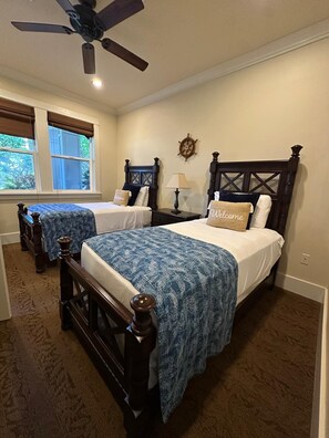 A bedroom with two beds, a ceiling fan, a ship's wheel decoration, and a window with a view of greenery. - 4BR I Ground Floor Luxury Penthouse at The Villas | F100 (Koloa)