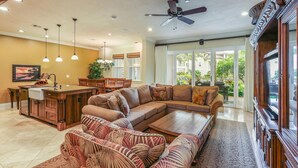 A spacious living room with a large sectional sofa, a dining area with wooden chairs, a kitchen island, and a ceiling fan. - 4BR I Ground Floor Luxury Penthouse at The Villas | F100 (Koloa)