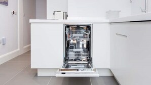 Une cuisine moderne dotée d’un lave-vaisselle encastré, de meubles blancs et d’un robinet en acier inoxydable.