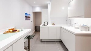Une cuisine moderne avec des meubles blancs, un plan de travail doté d’une cloison en verre et un petit coin repas avec une assiette de nourriture et une tasse.