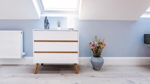 Une chambre moderne avec une lucarne, une commode blanche à rayures horizontales, une petite plante et un vase de fleurs.