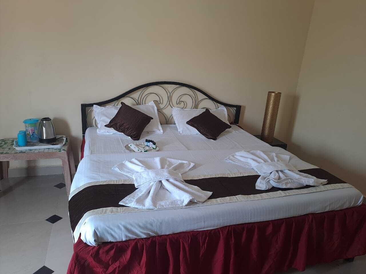 Una cama bien hecha con falda roja, almohadas blancas y marrones, y una toalla blanca doblada sobre la cama.