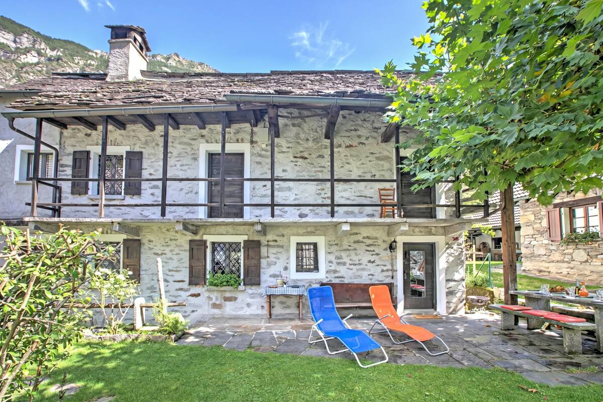 A two-story stone building with a balcony, outdoor seating, and a stone fireplace.
