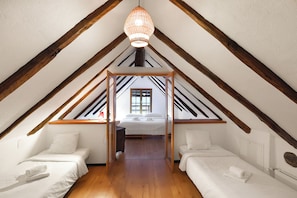 A room with two beds, wooden beams, a hanging light fixture, and a window. - Rustico al platano 2 (Sonogno)