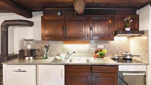 A kitchen with wooden cabinets, a granite countertop, a stainless steel sink, a dishwasher, and a built-in oven. - Rustico al platano 2 (Sonogno)