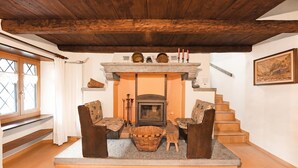 A cozy room with a fireplace, wooden furniture, a staircase, and a window with curtains. - Rustico al platano 2 (Sonogno)