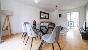 Ein modernes Wohnzimmer mit einem Glastisch, grau gepolsterten Sesseln, einer Stehlampe und einem großen Spiegel an der Wand.