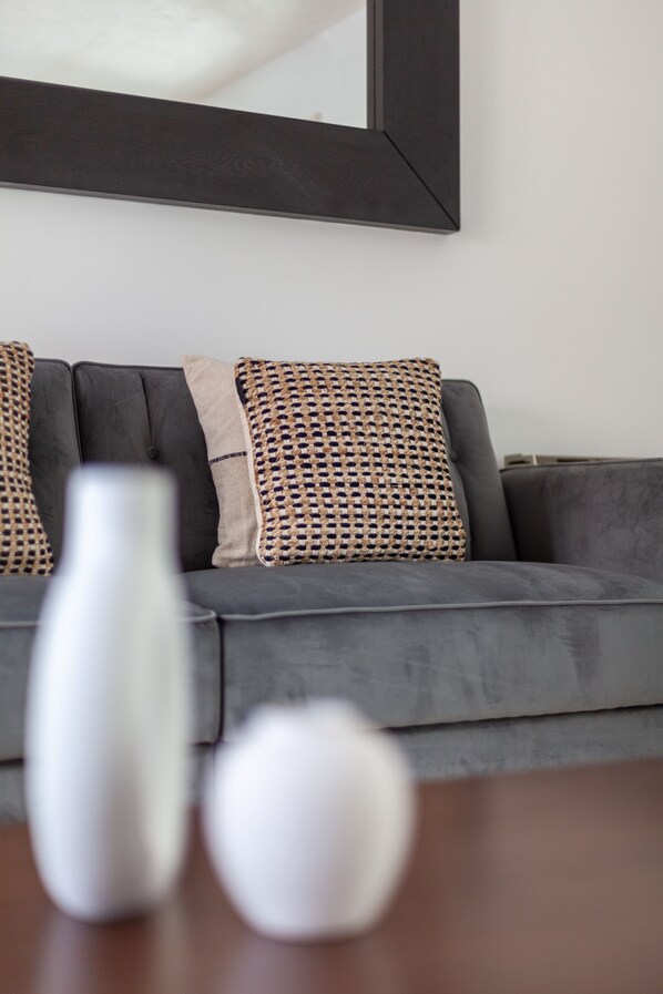 A modern living room with a grey sofa, patterned cushions, a white vase, and a round white object on a wooden table.