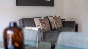 Ein modernes Wohnzimmer mit einem grauen Sofa, gemusterten Kissen und einem großen Spiegel an der Wand.