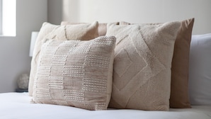 Ein ordentlich bezogenes Bett mit beige farbenen Bettwaren und einem gerahmten Kunstwerk an der Wand.
