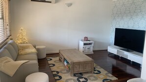 Un salon comprenant un canapé, un pouf, une table basse, un téléviseur et des luminaires décoratifs.