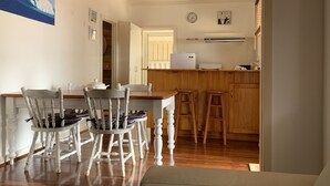 Un coin repas avec des chaises en bois blanches, une table en bois et une cuisine en arrière-plan.
